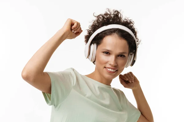 年轻的微笑的女人一边听着音乐一边带着耳机在白色背景下跳舞 — 图库照片