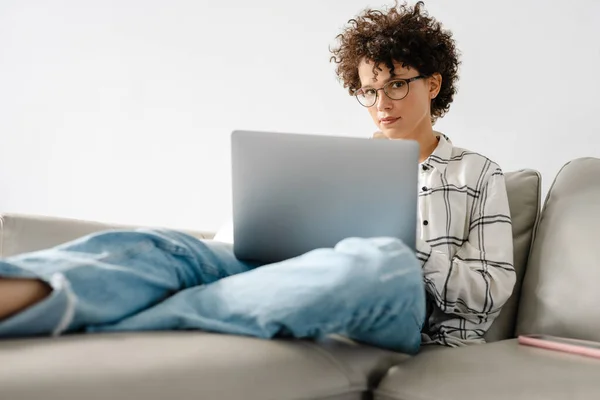 Jonge Krullende Vrouw Met Behulp Van Laptop Terwijl Zitten Bank — Stockfoto