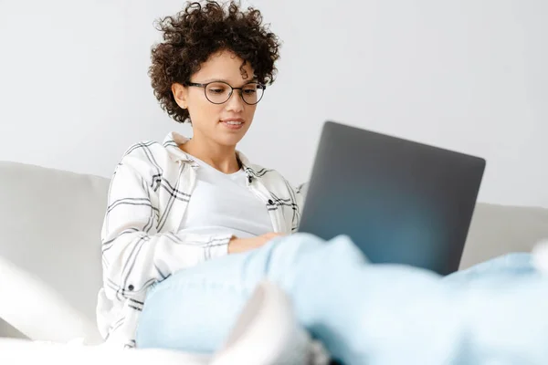 Jonge Krullende Vrouw Met Behulp Van Laptop Terwijl Zitten Bank — Stockfoto