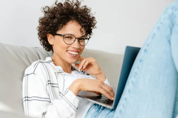 Jonge Krullende Vrouw Met Behulp Van Laptop Terwijl Zitten Bank — Stockfoto