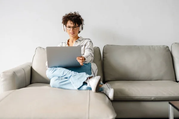 Jong Krullend Vrouw Hoofdtelefoon Met Behulp Van Laptop Terwijl Zitten — Stockfoto