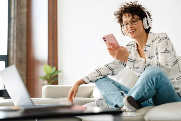 Ung Lockig Kvinna Hörlurar Använder Laptop Och Mobiltelefon Medan Sitter — Stockfoto