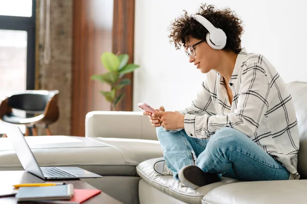 Mulher Encaracolado Jovem Fones Ouvido Usando Laptop Celular Enquanto Sentado — Fotografia de Stock