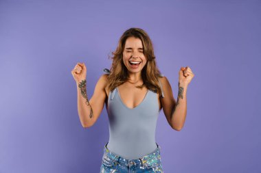 Heyecanlı genç bir kadın çığlık atarken kazanan jest yapıyor mor arka planda izole edilmiş.