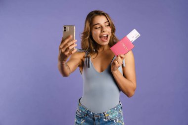 Pasaportunda mor arka planda izole edilmiş biletlerle selfie çeken genç beyaz kadın.