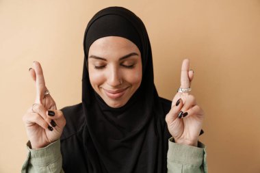 Olumlu Müslüman kadının portresi turuncu stüdyoda dikilirken kapalı gözlerle dua ediyor.