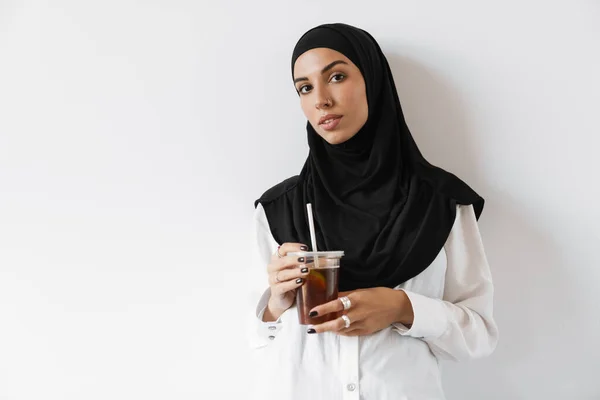 一名自信的穆斯林妇女 头戴头巾 手持塑料杯 站在白色的工作室里看着摄像机 — 图库照片