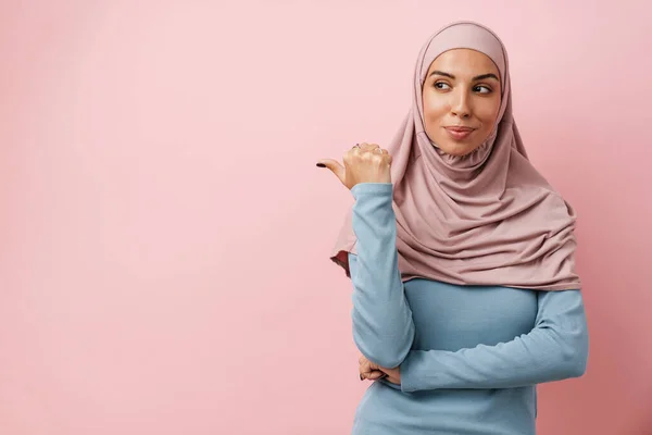 Pozytywna Muzułmanka Różowym Hidżabie Wskazująca Przestrzeń Kopiowania Spoglądająca Bok Różowym — Zdjęcie stockowe