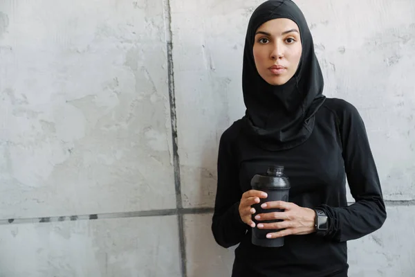 Młoda Muzułmanka Hidżabie Stojąca Butelką Wody Pomieszczeniu — Zdjęcie stockowe