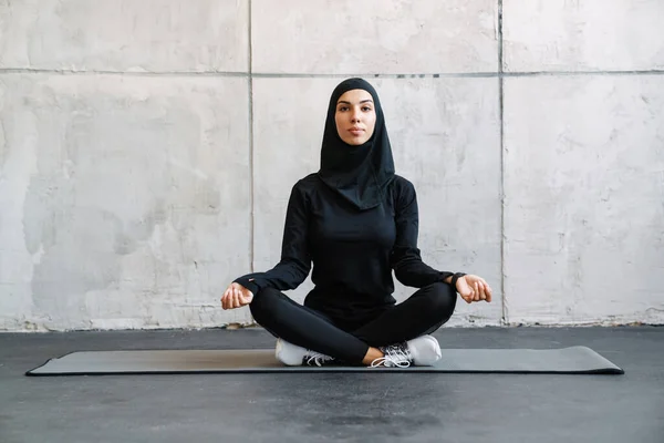 Młoda Muzułmanka Hidżabie Medytuje Siedząc Macie Fitness Domu — Zdjęcie stockowe