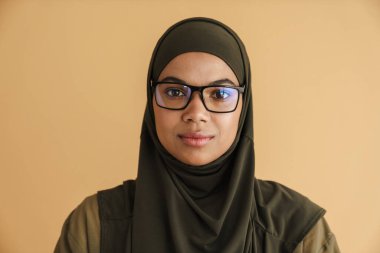 Siyah Müslüman kadın tesettürde poz veriyor ve bej arka planda izole kameraya bakıyor.