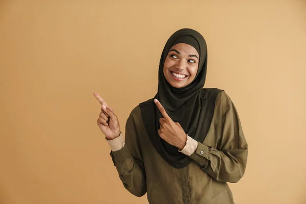头戴头巾 面带微笑 指指点点的黑人穆斯林妇女 与米色背景隔离在一边 — 图库照片