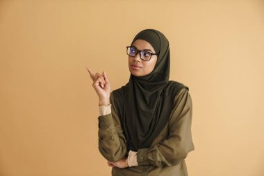 tesettürlü siyah müslüman kadın gülümseyen ve işaret eden bej arka planda izole edilmiş bir parmak.