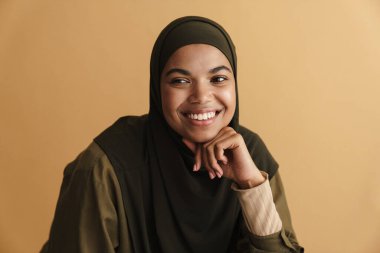 tesettürlü siyah müslüman kadın gülümsüyor ve bej arka planda soyutlanmış bir kenara bakıyor.