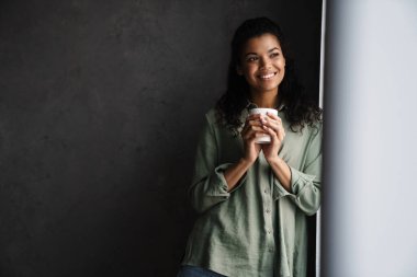 İçerde kahve içerken gülümseyen siyah bir kadın.