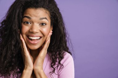 Genç siyah heyecanlı kadın mor arka planda izole edilmiş bir şekilde el kol hareketi yapıyor ve kameraya bakıyor.