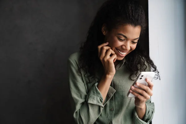 Svart Ung Kvinne Ler Når Hun Bruker Mobiltelefon Inne – stockfoto