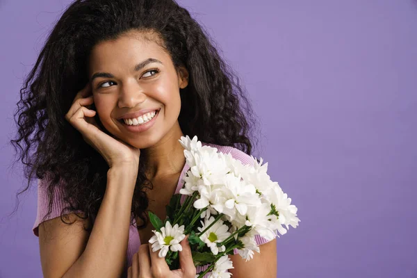 Young black woman smiling while posing with chrysanthemum isolated over purple background