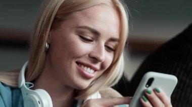 Kulaklıklı mutlu bir kadının yakın plan görüntüsü dairesinde oturan telefonunu kullanıyor.