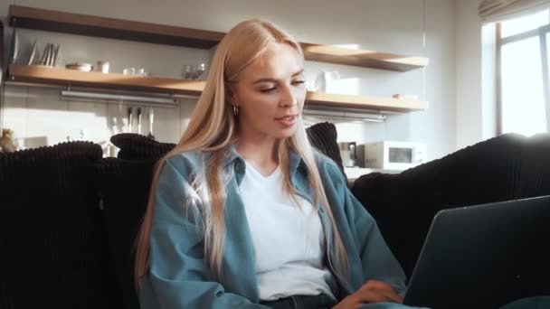 Sarışın Bir Kadını Evdeki Koltukta Dizüstü Bilgisayarını Kullanıyor — Stok video