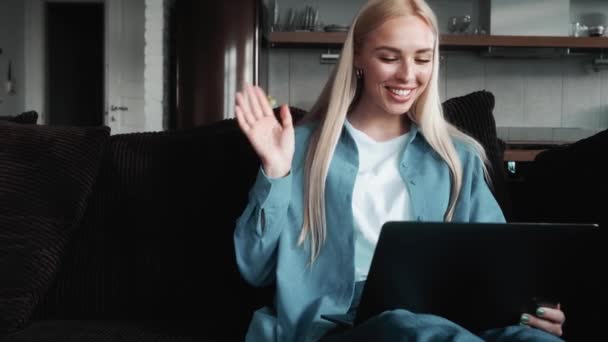 Szczęśliwa Blondynka Pracuje Podczas Rozmowy Wideo Machając Ręką Kanapie Apartamentach — Wideo stockowe