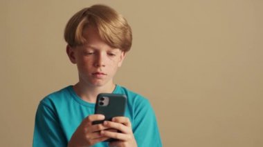 Ciddi bir çocuk telefonuyla stüdyodaki bej arkaplanı kullanıyor.