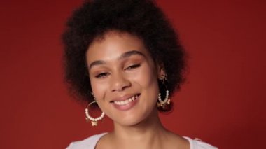 Güzel bir Afrikalı Amerikalı kadının yakın çekim görüntüsü. Kameraya bakıyor. Stüdyonun kırmızı duvarında tek başına duruyor.