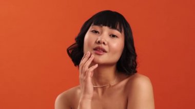 Çekici, yarı çıplak bir Asyalı kadının, stüdyodaki turuncu duvarın üzerinden tenine dokunurken kameraya yakın çekim görüntüsü.