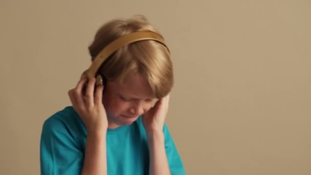 Приємний Маленький Хлопчик Слухає Музику Використовуючи Навушники Ізольовані Бежевому Фоні — стокове відео