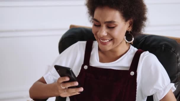 Uma Bela Mulher Afro Americana Usando Seu Celular Rindo Sentada — Vídeo de Stock