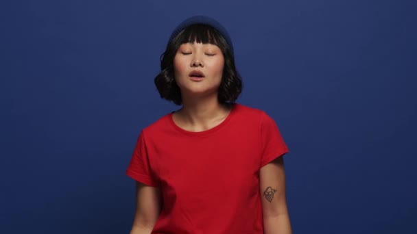 一个面带微笑的亚洲女人站在工作室的蓝色墙壁上做着一个比较松懈的动作 — 图库视频影像