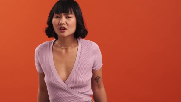 一位严肃的亚洲女人正在偷听观众们的谈话 同时对着摄影棚里被隔离在橙色墙上的摄像机做消极的手势 — 图库视频影像