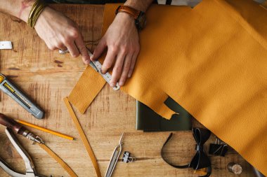 Beyaz zanaatkar atölyedeki ahşap masada deriyle çalışıyor.