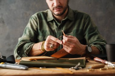 Beyaz zanaatkar atölyede deri cüzdan yaparken dikiş dikiyor.