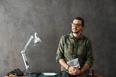 Sakallı beyaz zanaatkar atölyesinde deri debriyajla dikiliyor.