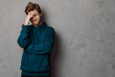 Beyaz kızıl saçlı, sakallı, gülümseyen ve yüzünü kaplayan adam gri arka planda soyutlanmış.