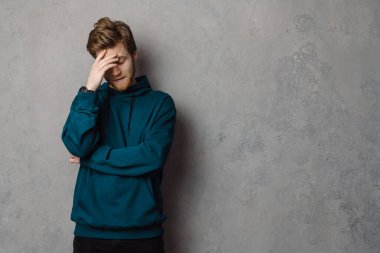 Sakallı, beyaz, kızıl saçlı adam yüzünü gri arka planda gizliyor.