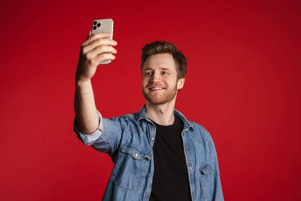 Kırmızı Duvarın Arkasında Dikilip Selfie Çeken Sıradan Giyinmiş Mutlu Genç — Stok fotoğraf
