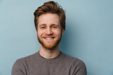 Gri arka planda dikilip kameraya bakan mutlu beyaz bir adamın portresi.