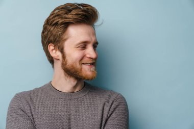 Sakallı beyaz kızıl adam gülümsüyor ve mavi arka planda tek başına bakıyor.