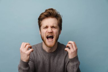 Beyaz kızıl sakallı adam çığlık atıyor ve mavi arka planda izole bir şekilde kameraya işaret ediyor.
