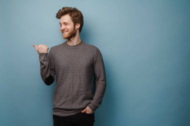 Beyaz kızıl adam gülümserken mavi arka planda yalnız bir şekilde işaret ediyor.