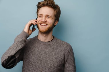 Gri arka planda durup cep telefonuyla konuşan mutlu beyaz bir adamın portresi.