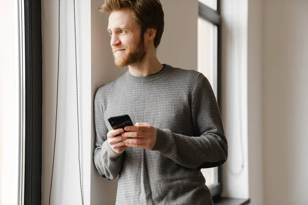 Ginger Young Man Using Mobile Phone While Leaning Wall Indoors — Stock Photo, Image