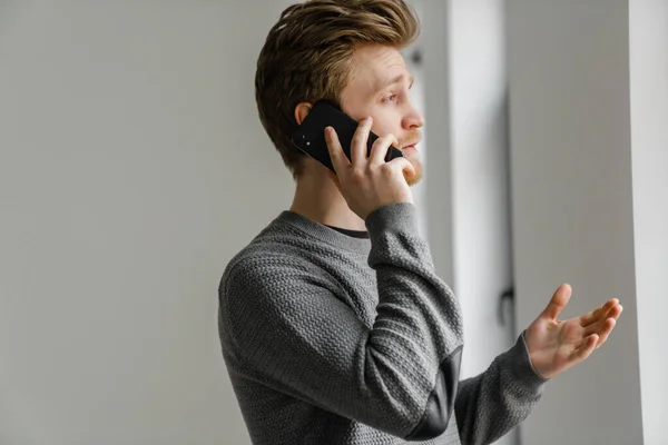 Рыжий Молодой Человек Разговаривает Мобильному Телефону Стоя Помещении — стоковое фото