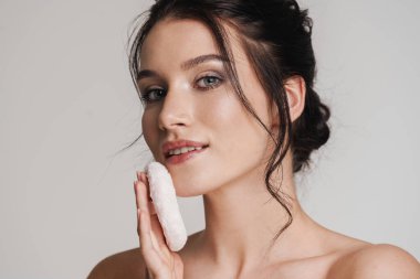 Kahverengi saçlı genç beyaz kadın elinde pudra ponponu tutuyordu gri arka planda izole edilmişti.