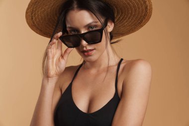 Hasır şapkalı genç esmer kadın poz veriyor ve izole edilmiş bej arka plana bakıyor.