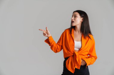 Genç esmer kadın gri arka planda izole edilmiş kamerayı işaret ediyor.