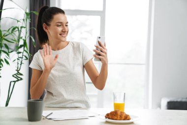 Gülümseyen kadın evde kahvaltı yaparken cep telefonuyla selfie çekiyor.