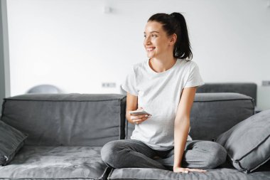 Avrupa 'dan gülümseyen bir kadın evdeki koltukta otururken cep telefonu kullanıyor.